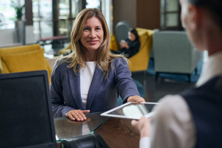 Smiling woman using digital tablet during her registration in the hotel