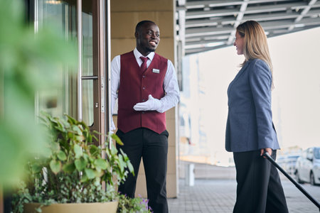 African American doorman greeting guest and opening door for her while she entering in the hotelの写真素材