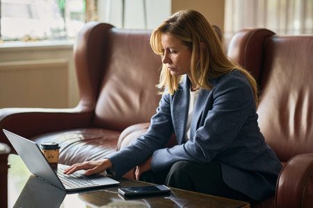 Businesswoman working online on laptop while sitting on sofa in lobby of the hotelの写真素材