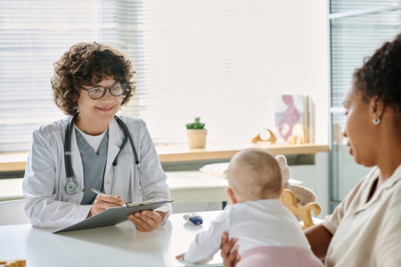 Professional pediatrician writing prescription while mother sitting with baby at the tableの写真素材