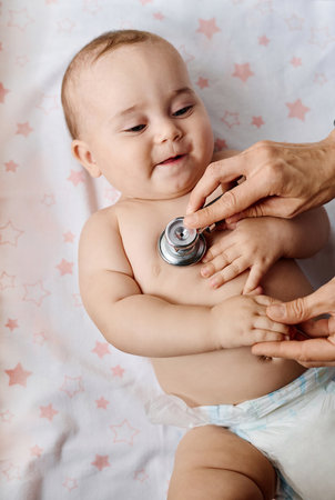 High angle view of baby lying on couch while doctor listening to hearbeat of babyの写真素材