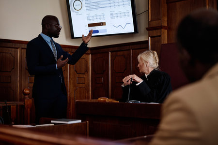 Confident African American lawyer in formalwear pointing at screen with summary of results while explaining data to mature female judgeの写真素材