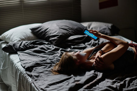 Side view of teenage girl with mobile phone reading cyberbullying messages sent by anonymous user which make her feeling upsetの写真素材