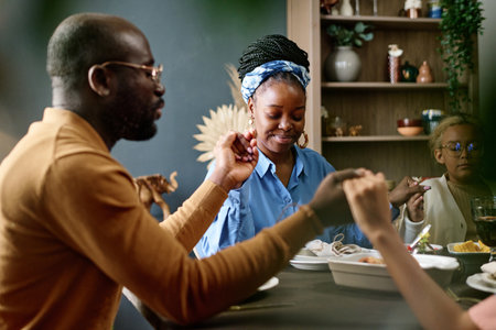 Happy young woman sitting between her husband and daughter and holding by their hands during...