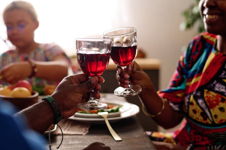 Hands of young African American couple with red homemade wine clinking with wineglasses while...