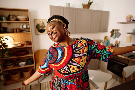 Young ecstatic woman in ethnic dress performing dance in front of camera while celebrating African American holiday in home environmentの写真素材