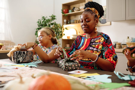Happy young African American woman and her daughter packing boxes with presents while preparing for kwanzaa celebration with familyの写真素材