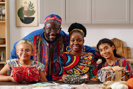 Happy young African American family of four in national costumes looking at camera while woman and...