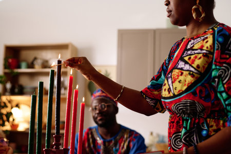 Cropped shot of African American woman in ethnic dress burning kwanzaa candles while standing in front of camera against her husbandの写真素材