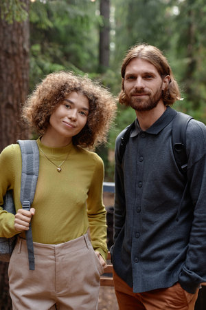 Vertical portrait of young couple looking at camera while hiking in the forest