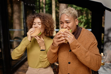 Young women eating homemade burgers at barbecue partyの写真素材