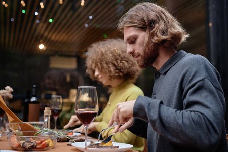 Young couple eating grilled meat at table at picnic on fresh airの写真素材