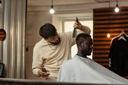 Professional hairdresser using comb and trimmer to make haircut for customer in hair salonの写真素材