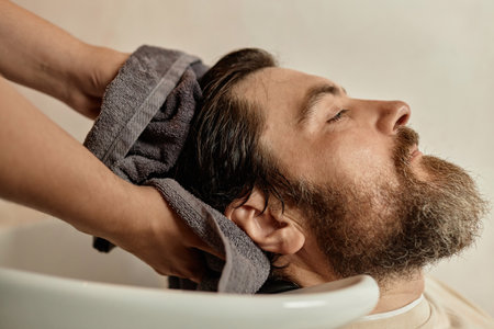 Young bearded man washing his hair in barber shop before haircut