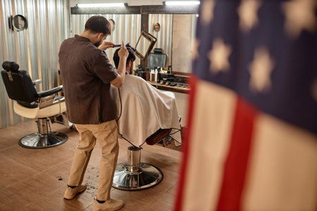 Rear view of young professional barber making haircut to customer in barber shopの写真素材