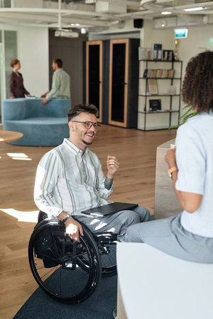 Vertical image of man with disability talking to his colleague while they sitting in office hallの写真素材