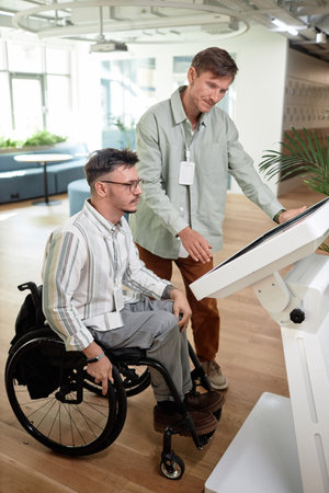 Vertical image of man helping to make online entry for man with disability in office hallの写真素材