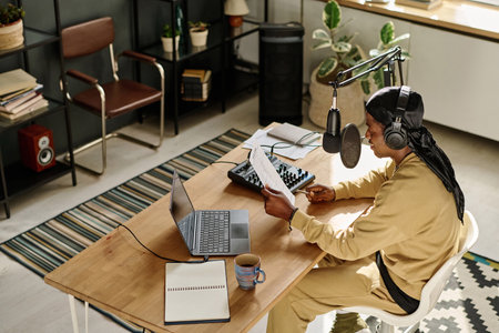 Above angle of African American guy reading text on paper while sitting by desk in front of...