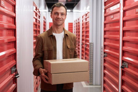 Smiling mature man with cardboard box standing in self-storage where he rents unitの写真素材