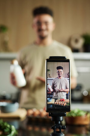 Closeup of smartphone filming smiling young middle eastern chef showing bottle of milk to camera...