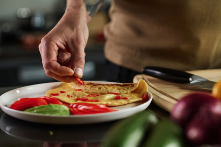 Closeup of hand of unrecognizable man placing slice of chili pepper on omeletの写真素材