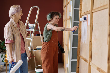 Happy girls in workwear painting walls in the room during repair in their new houseの写真素材