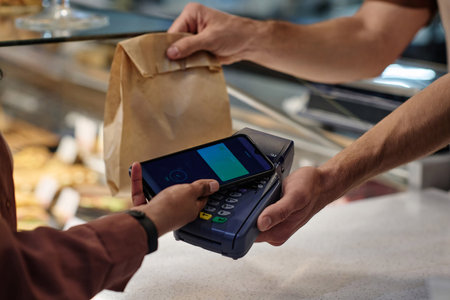 Unknown customer paying for her purchase with smartphone, unrecognizable cashier receiving payment