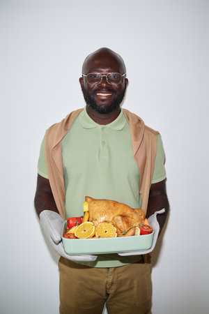 Young african american man standing with tray with poultry and vegetables smiling at cameraの写真素材