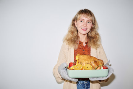 Caucasian woman holding tray with roasted turkey standing against white background smiling at camera