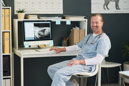 Joyful veterinarian posing at his workplace in veterinary office sitting at deskの写真素材
