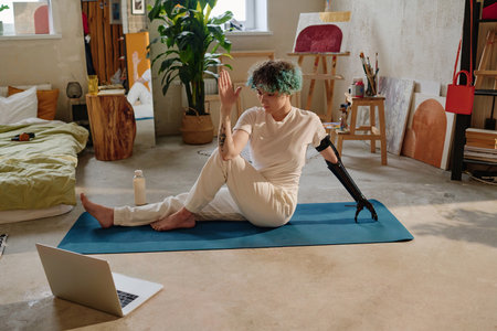 Teenage girl with prosthetic arm following tutorial on laptop when doing twist yoga pose