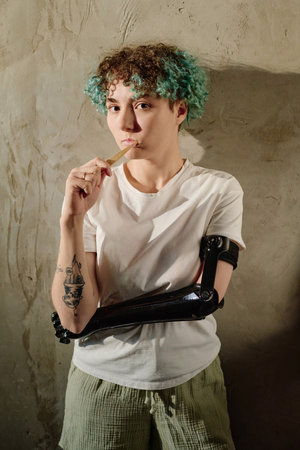 Portrait of young woman with prosthetic arm brushing teeth in morningの写真素材