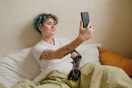 Joyful girl with person with disability sitting in bed and video calling friend or family member