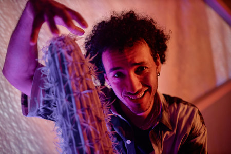 Young man posing with cactus demonstrating its length with his hand and smiling at camera