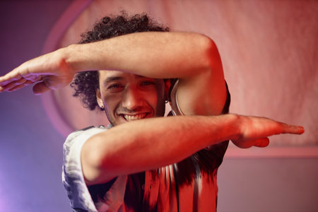 Young smiling man posing for camera with arms bent at elbows in front of his faceの写真素材