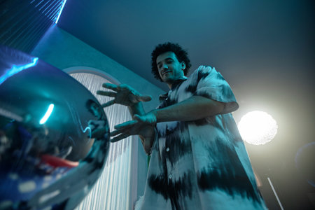 Low angle shot of stylish man posing next to shiny art object moving his hands