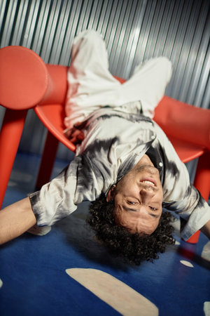 Young man laying upside down in coral armchair looking at camera