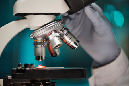 Closeup of hand adjusting microscope to analyze piece of lab-grown meat under lens