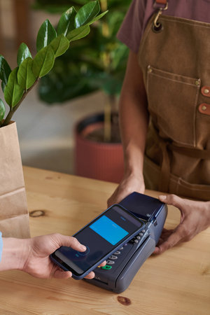 Woman paying for potted plant in shop using her mobile phone