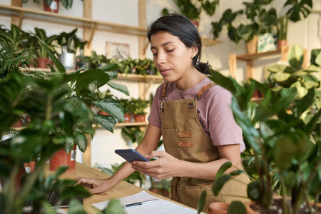 Hispanic plant shop employee scrolling through information on laptop and smartphoneの写真素材