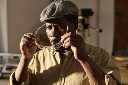 Portrait of African American senior carpenter putting on protective glasses in sunlit workshopの写真素材