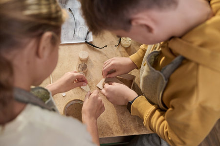 Top view closeup of two kids building wooden model together in carpenting workshop for children