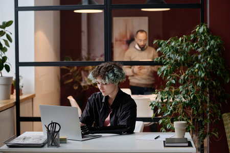 Girl with prosthetic arm typing on computer at desk in office, her colleague working on background