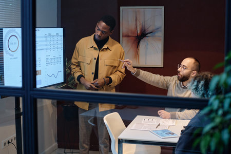 Colleagues discussing data presented on display in office conference roomの写真素材