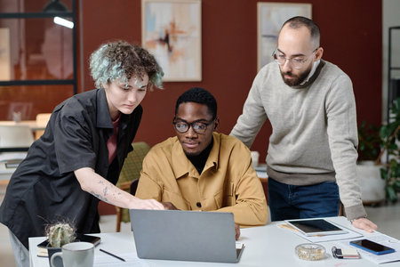 Young female office worker and her biracial male colleagues examining information on laptop screenの写真素材