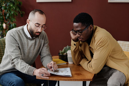 Middle eastern and african american male colleagues thoughtfully examining infographics in documentの写真素材