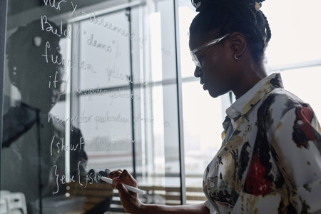 Young african american office employee writing code with white marker on glass boardの写真素材