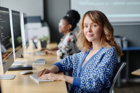 Caucasian female coder sitting at her desk working with data on computer and smiling at camera