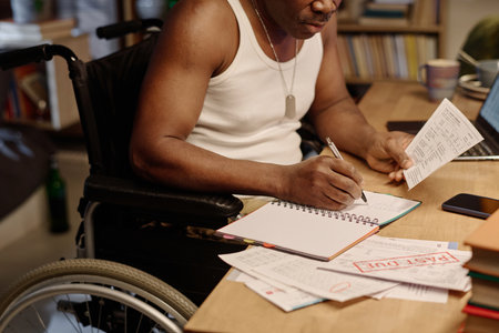 Unrecognizable black man in wheelchair writing information from piece of paper into his notebookの写真素材