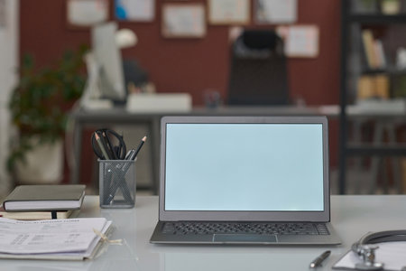 Laptop with white blank screen placed on hospital office desk amid equipment of professional doctorの写真素材